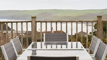 Een tafel en stoelen op een balkon met uitzicht op een kustlandschap met heuvels en de zee.