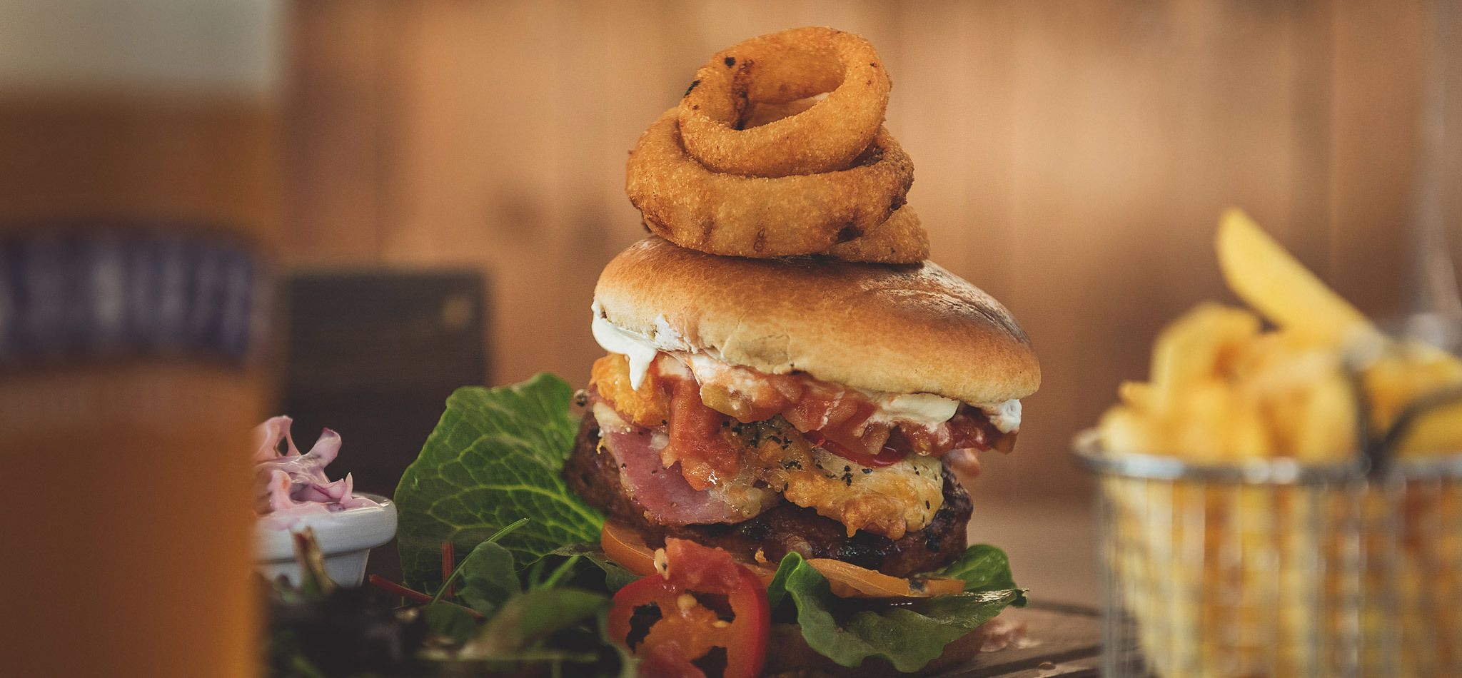 Un hamburger garni d’un oignon frit en forme d’anneau, servi avec des frites et une petite salade.