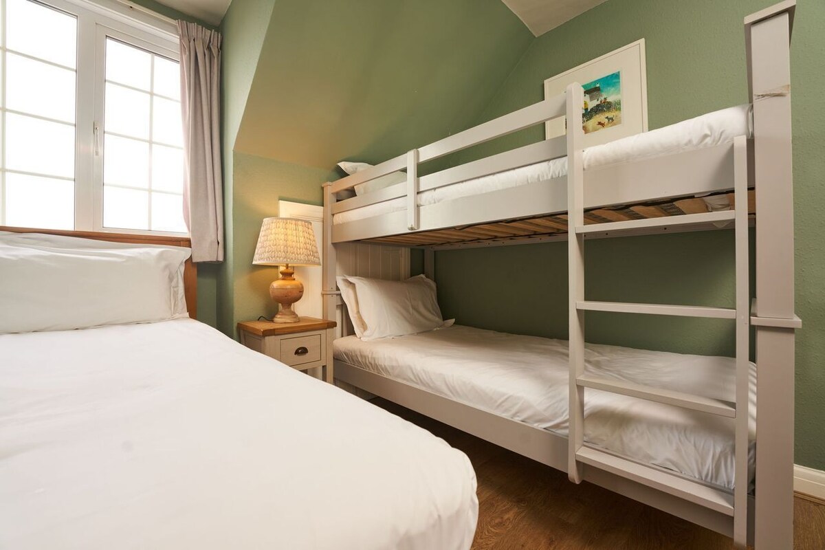 A room with bunk beds, a bedside table with a lamp, and a window with curtains.