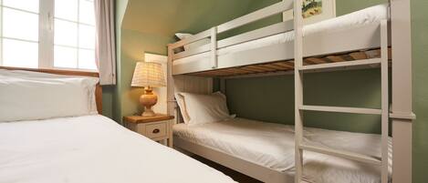 A room with bunk beds, a bedside table with a lamp, and a window with curtains.