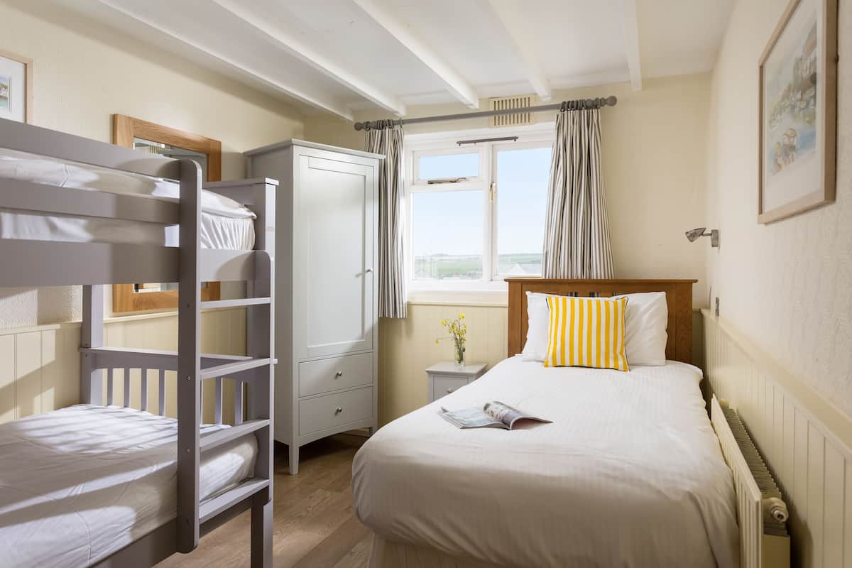 A bedroom with bunk beds, a single bed, a wardrobe, a nightstand, and a window with curtains.