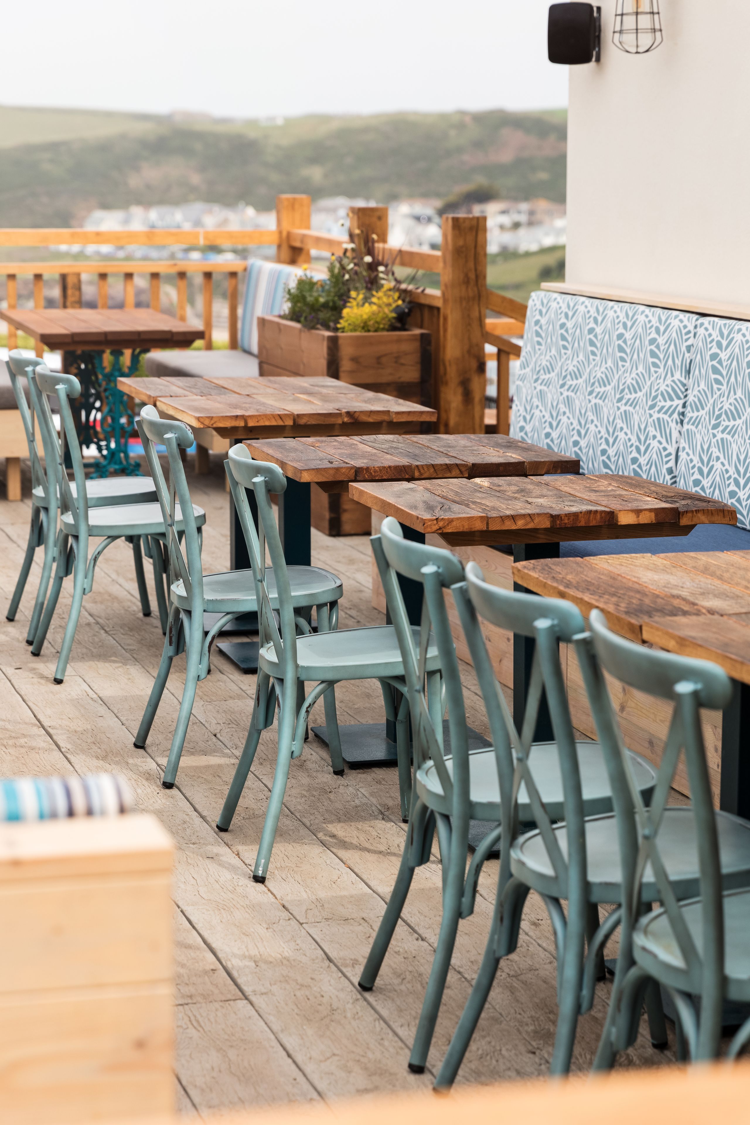 An outdoor dining area with wooden tables and metal chairs, overlooking a scenic view.