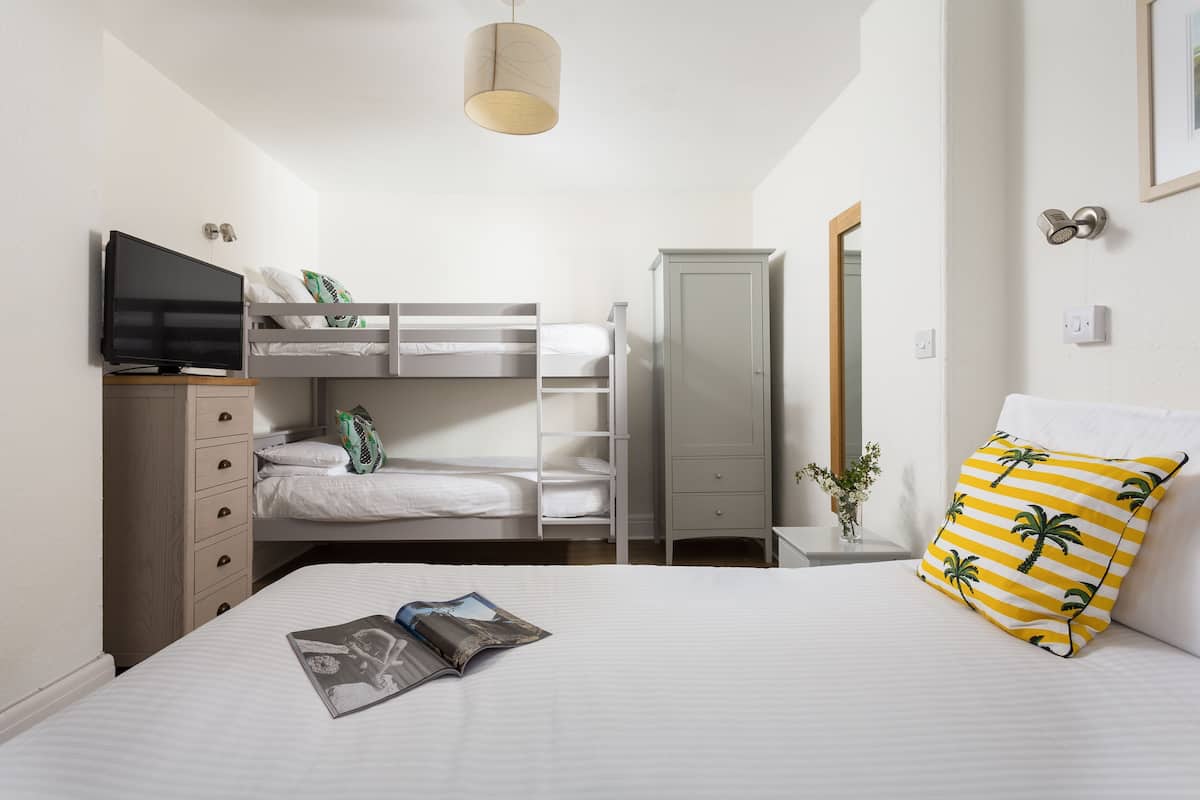 A bedroom with a bunk bed, a television, a wardrobe, and a bedside table with a magazine.