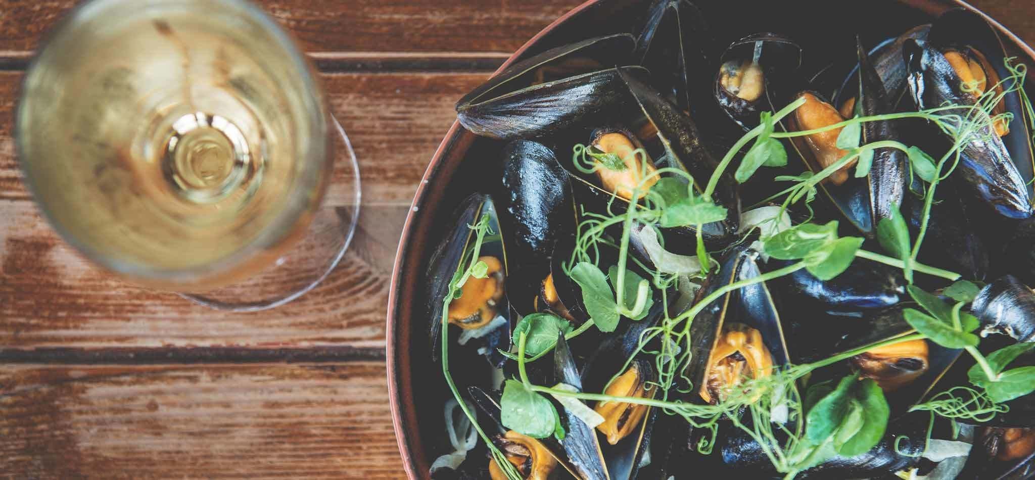 Un bol de moules et de légumes verts sur une table en bois.