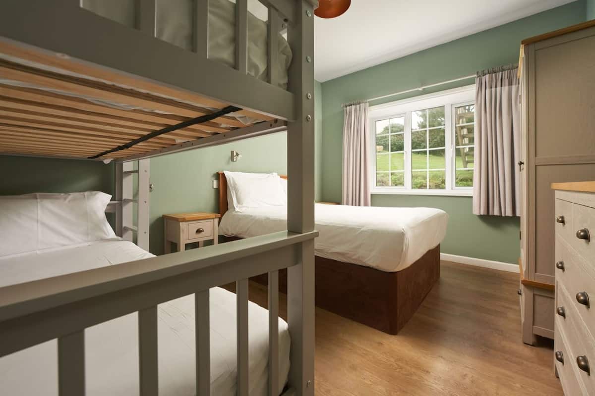 A bunk bed room with a wooden ceiling, a window with curtains, a dresser, and a nightstand.