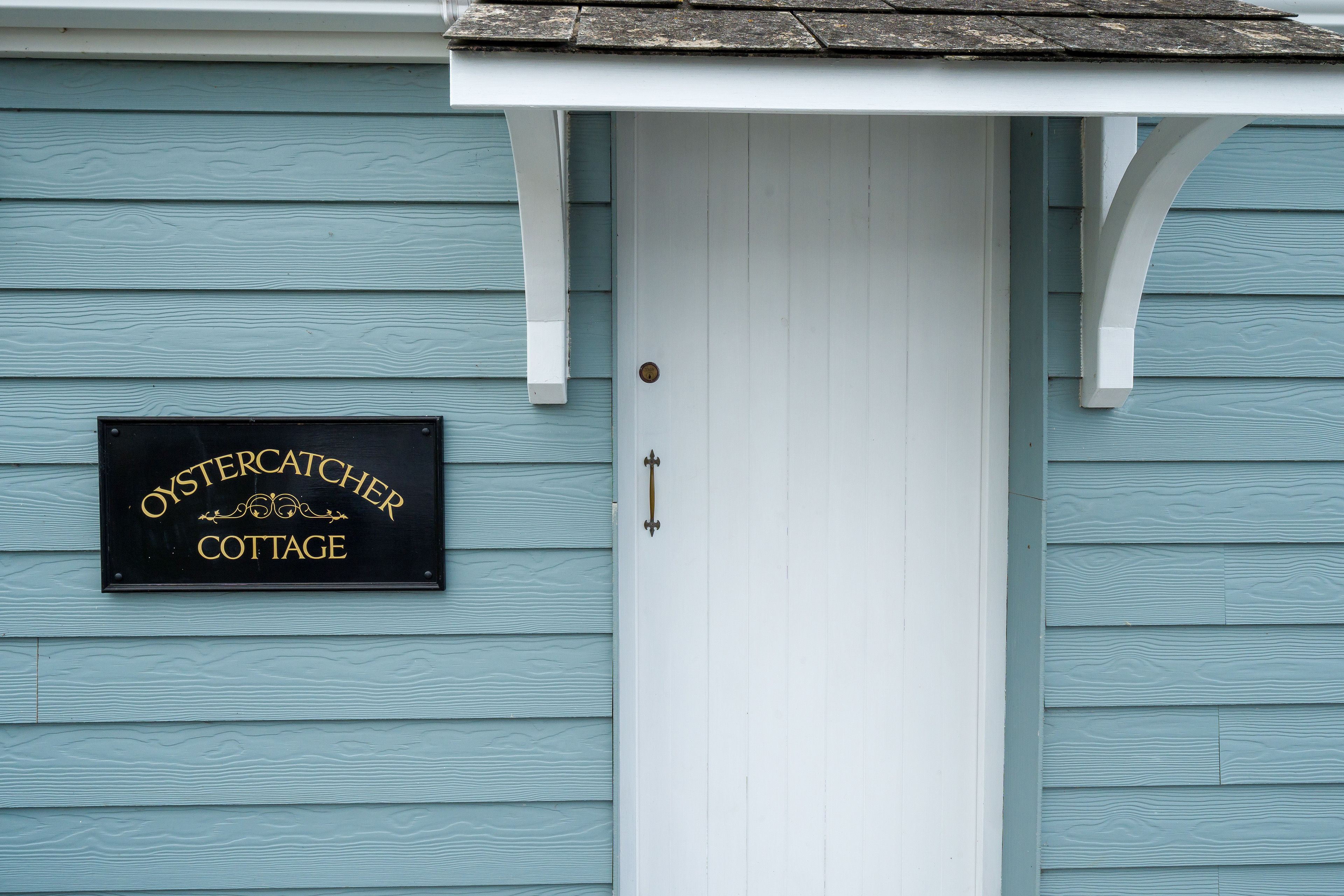 A cottage with a sign reading "OysterCatcher Cottage" mounted on the wall.