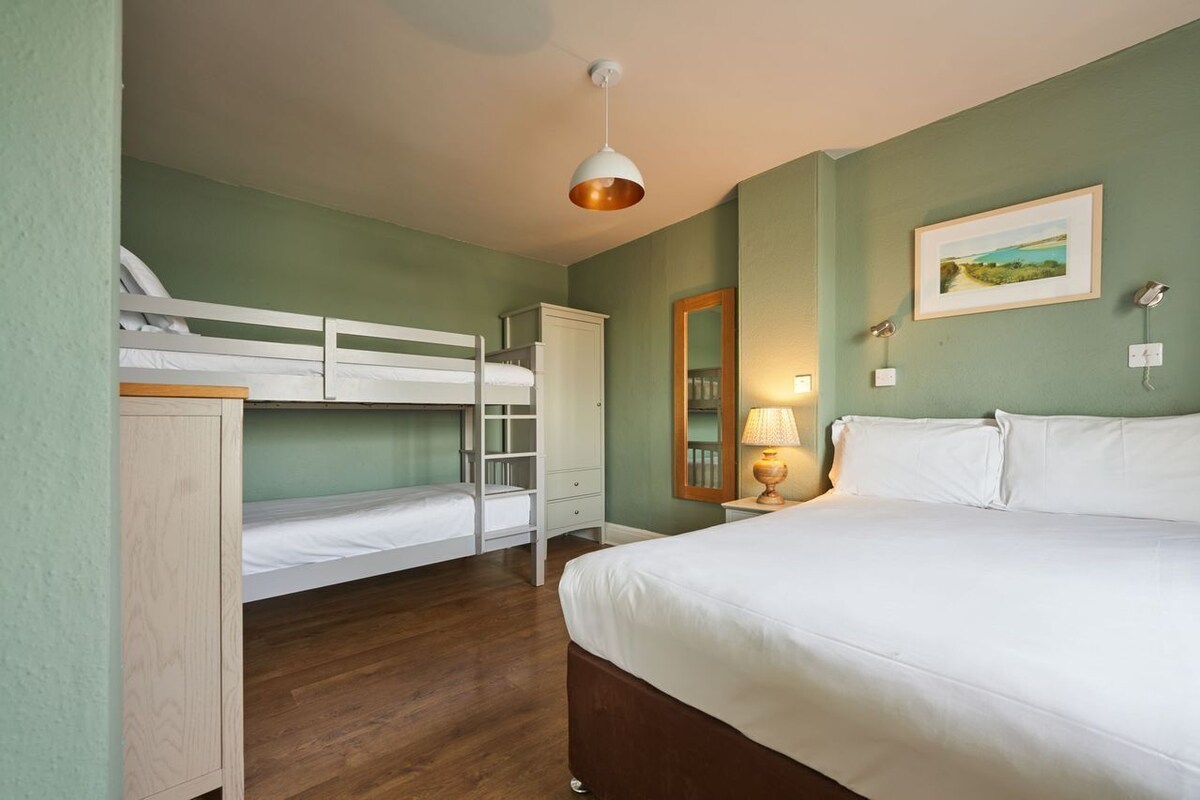 A bedroom with bunk beds, a single bed, a bedside lamp, a mirror, and a framed picture on the wall.
