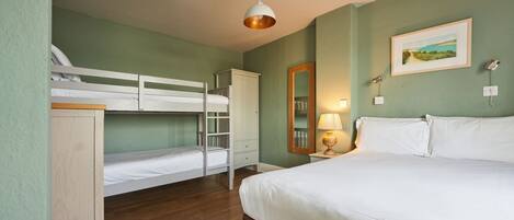 Een slaapkamer met stapelbedden, een enkele bed, een bedlampje, een spiegel en een lijst met een afbeelding aan de muur.