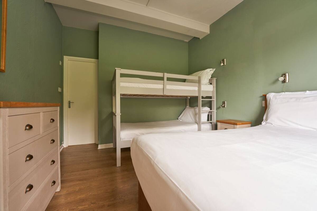 A bedroom with a bunk bed, a dresser with drawers, a bedside table, and a door.
