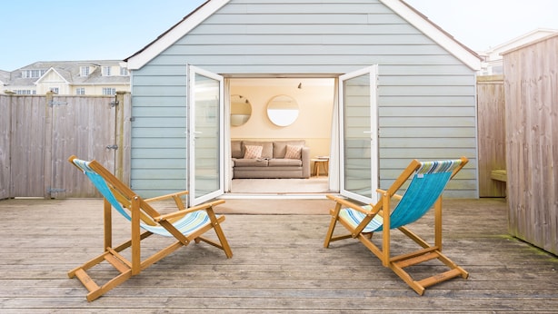 A wooden deck with two beach chairs and a view into a house with a sliding glass door. - Oystercatcher Apartments (Wadebridge)