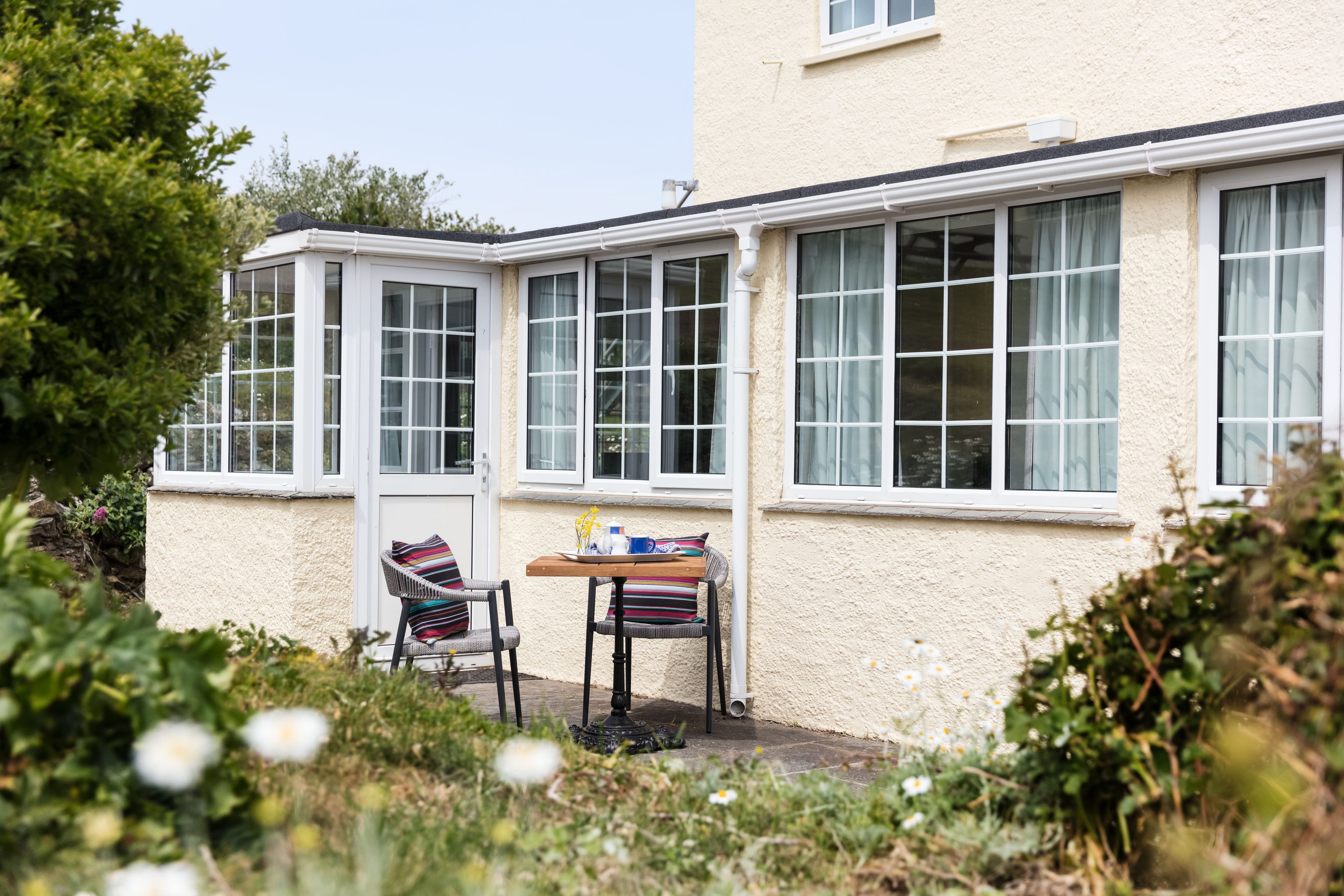A small patio area with a table and two chairs, a window with curtains, and a door.