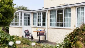 A small patio area with a table and two chairs, a window with curtains, and a door.