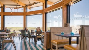 A spacious dining area with large windows, wooden beams, and striped flooring. - Oystercatcher Apartments (Wadebridge)
