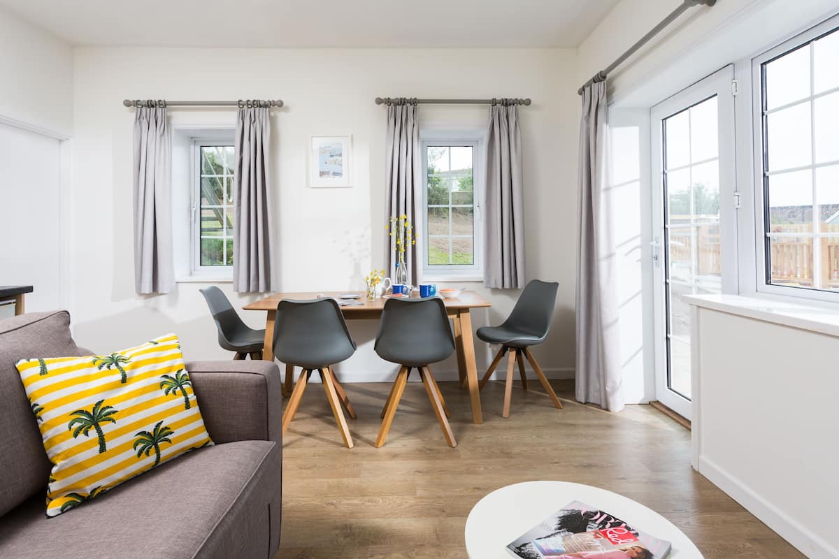 A modern living room with a sofa, a dining table with chairs, and large windows with curtains.
