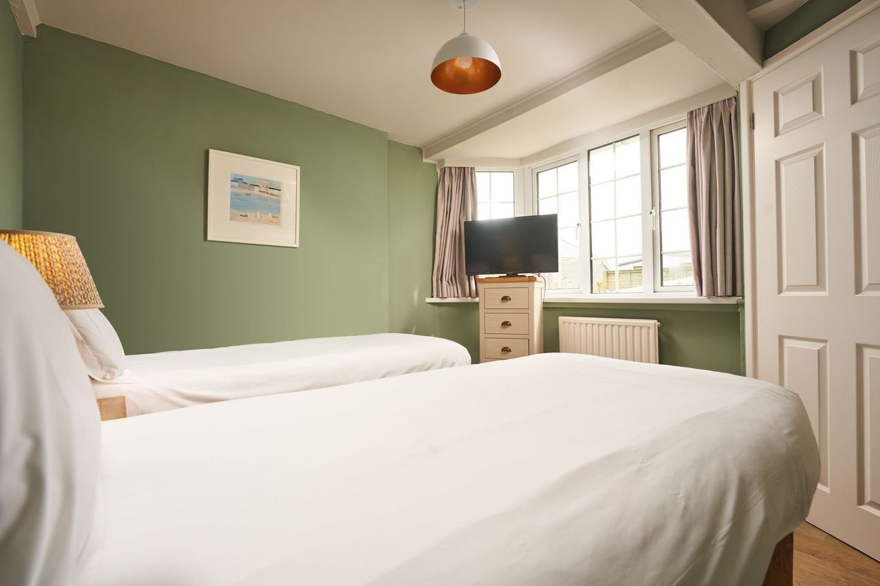 Une chambre avec deux lits, un téléviseur posé sur une commode et une fenêtre avec des rideaux.