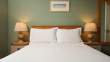 Una cama bien hecha con sábanas blancas, flanqueada por dos mesitas de noche con lámparas, frente a una pared verde con un cuadro enmarcado.