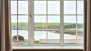 A view through a window with a grid pattern, overlooking a coastal landscape with hills and a beach. - Oystercatcher Apartments (Wadebridge)