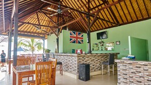 A covered outdoor seating area with wooden tables and chairs, a bar with a stone counter, and a British flag on the wall. - Scoobydoo Bungalow (Lembongan Island)