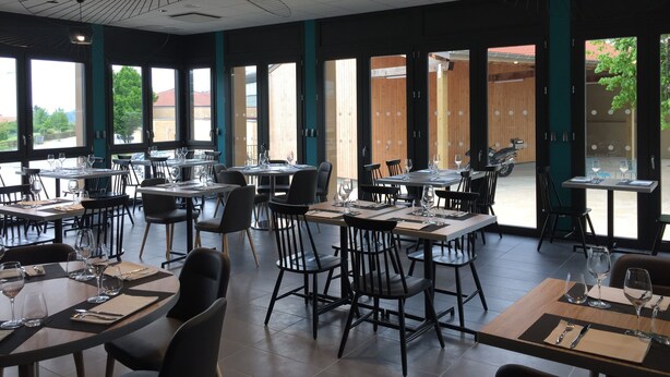 Ein Restaurant mit mehreren Tischen und Stühlen, großen Fenstern und einem modernen Deckenstil.