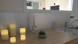 Eine moderne Küche mit einer Holzarbeitsplatte, einem Edelstahl-Spülbecken und einem Spiegel darüber. Vier beleuchtete Kerzen stehen auf der Arbeitsplatte und ein kleiner Blumentopf ist ebenfalls vorhanden.