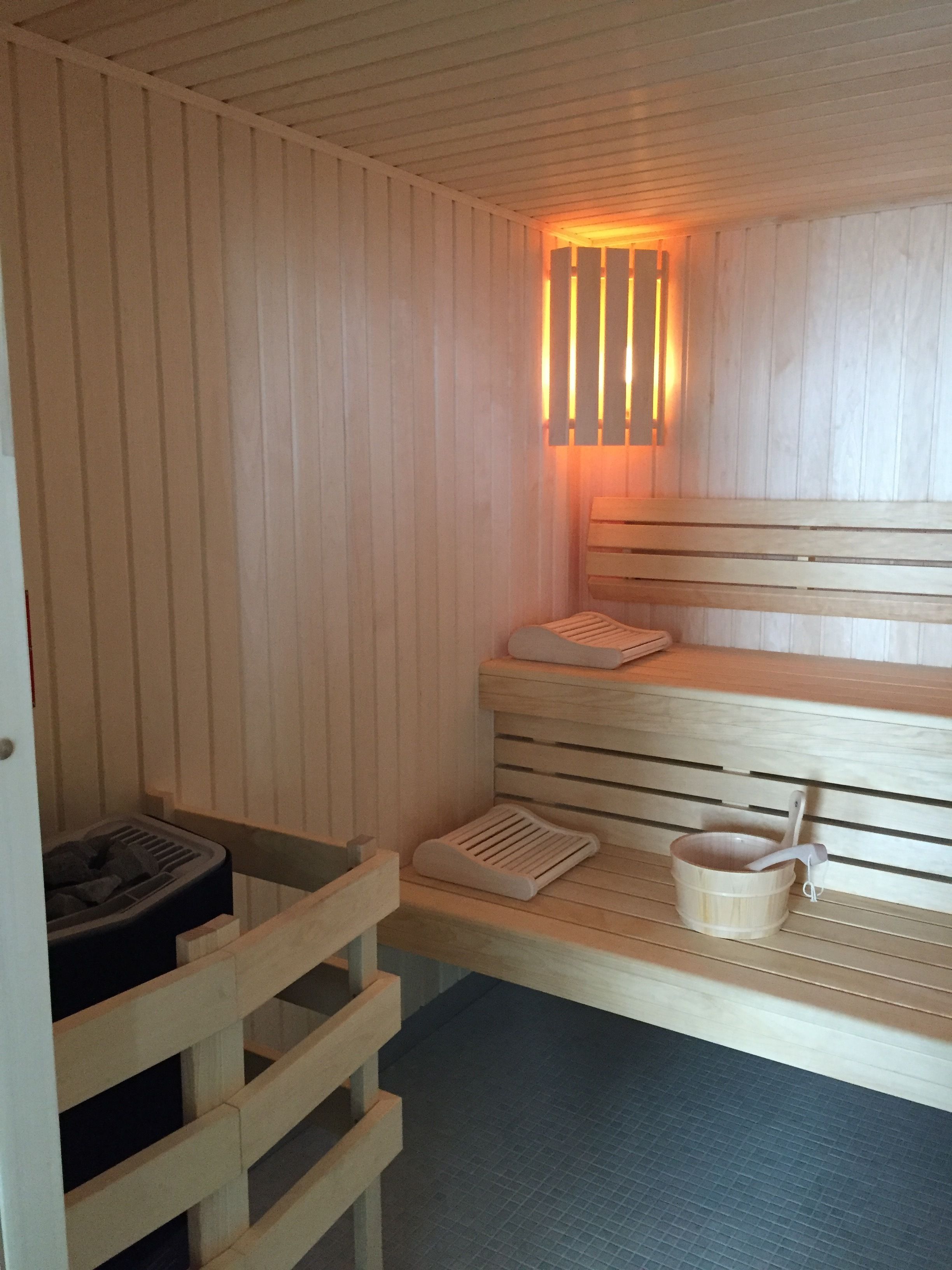 Een sauna met houten banken, een bankverwarmer en een emmer met een schuimspaan.