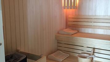 Een sauna met houten banken, een bankverwarmer en een emmer met een schuimspaan.