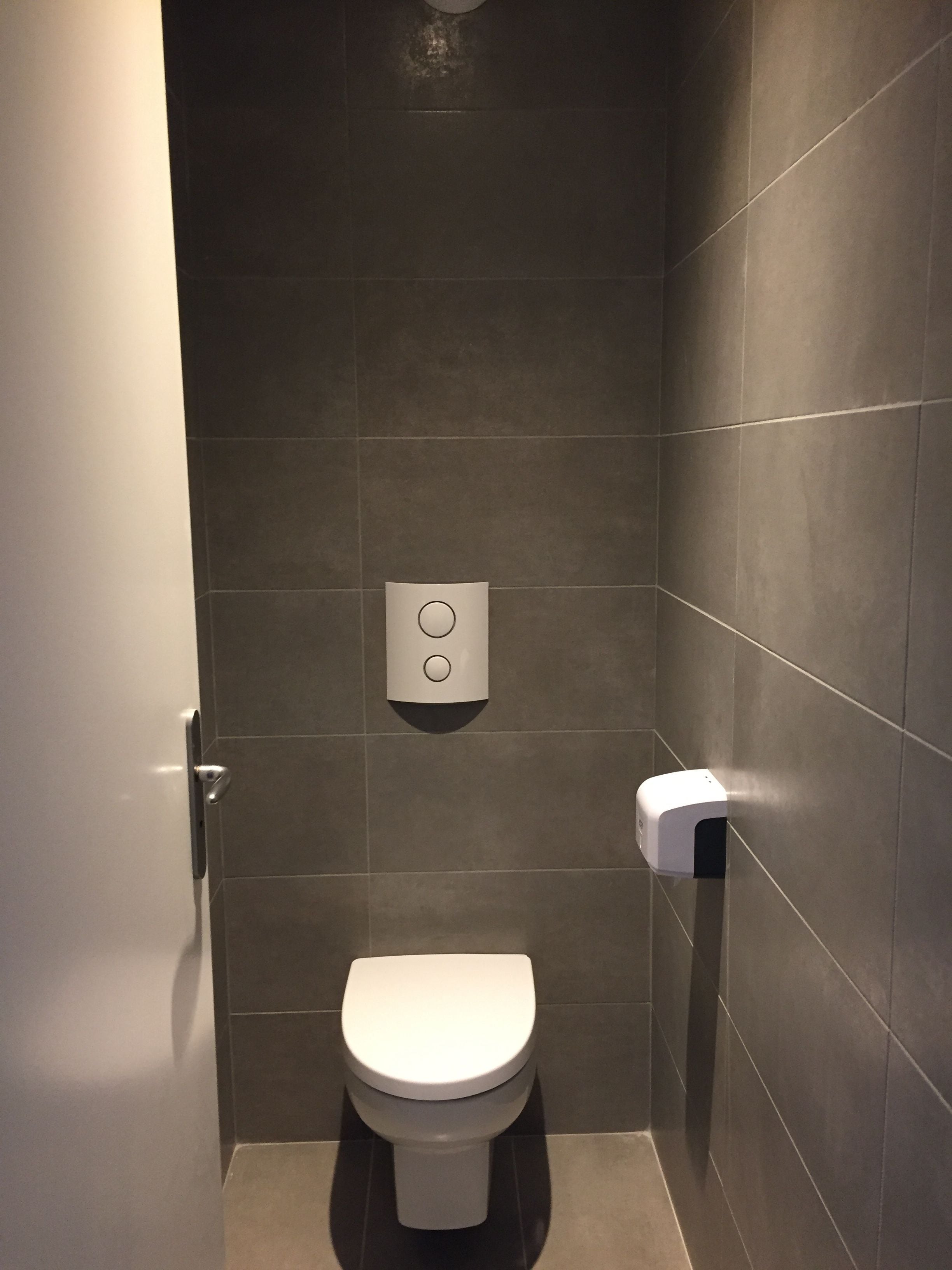 Un bagno piccolo e moderno con il water bianco, un distributore di carta assorbente e un erogatore di sapone a parete.