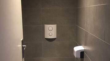 Un bagno piccolo e moderno con il water bianco, un distributore di carta assorbente e un erogatore di sapone a parete.