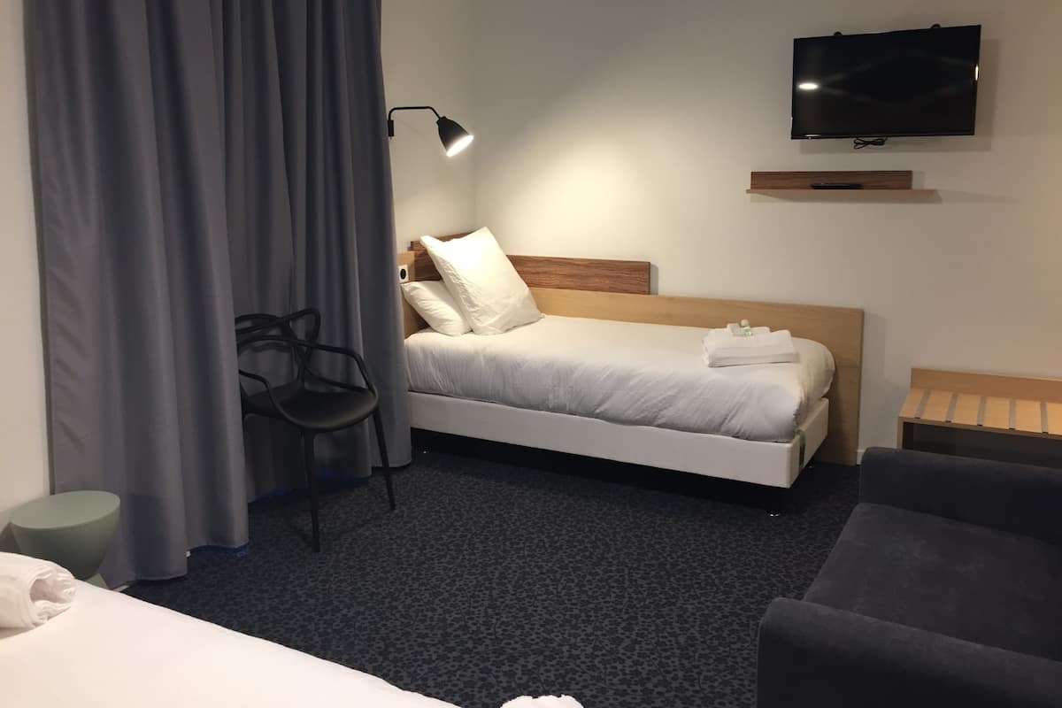 A hotel room with a bed, a TV mounted on the wall, a chair, and a small table.