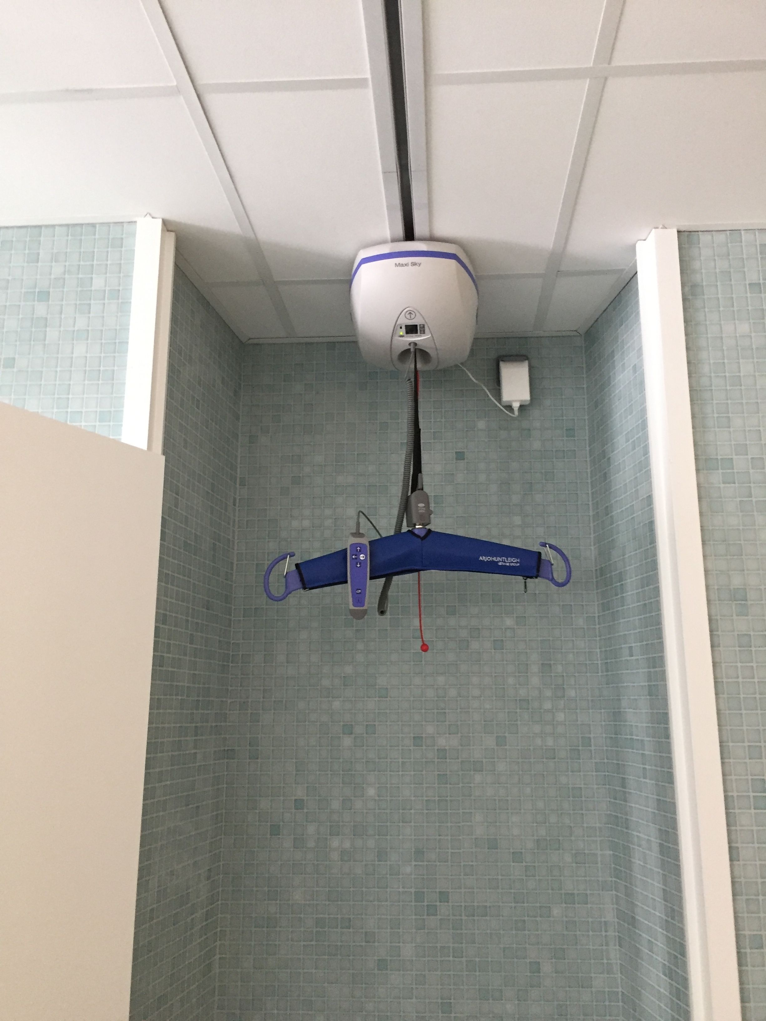 Un dispositivo fijado al techo, posiblemente un monitor de seguridad o calidad del aire, en una habitación con paredes de azulejos y techo blanco.