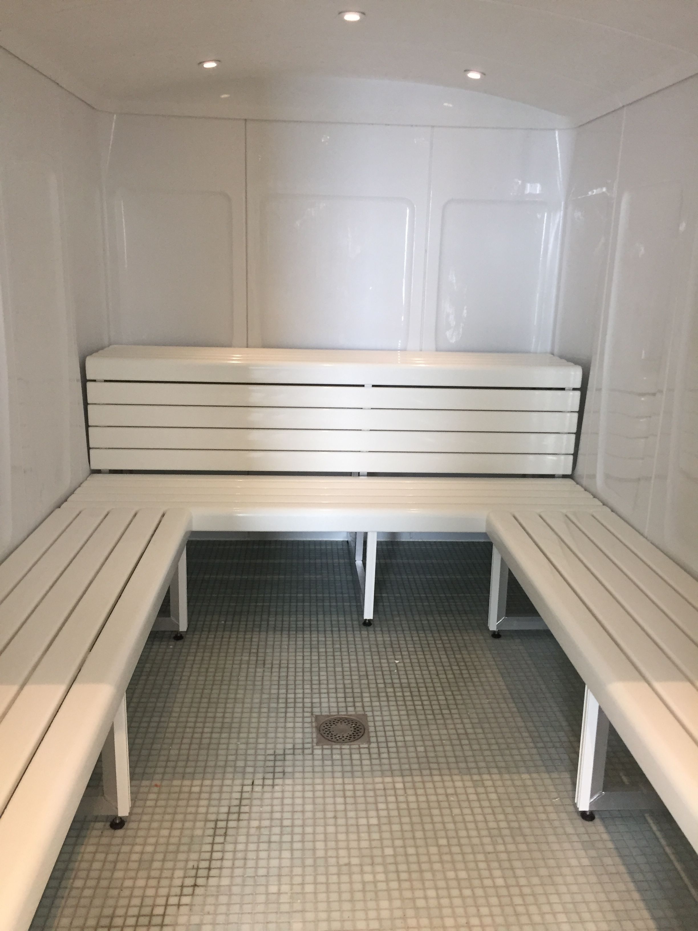 A sauna with a bench and two smaller benches, tiled floor, and a ceiling with recessed lighting.