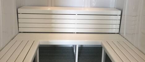 Una sauna con un banco y dos bancos más pequeños, suelo de azulejos e iluminación empotrada en el techo.