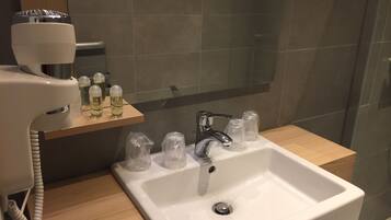 Un baño con un lavabo blanco, un espejo y un secador de pelo sobre una estantería de madera.