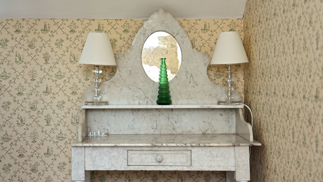 A vanity with a mirror, two lamps, and a green bottle.
