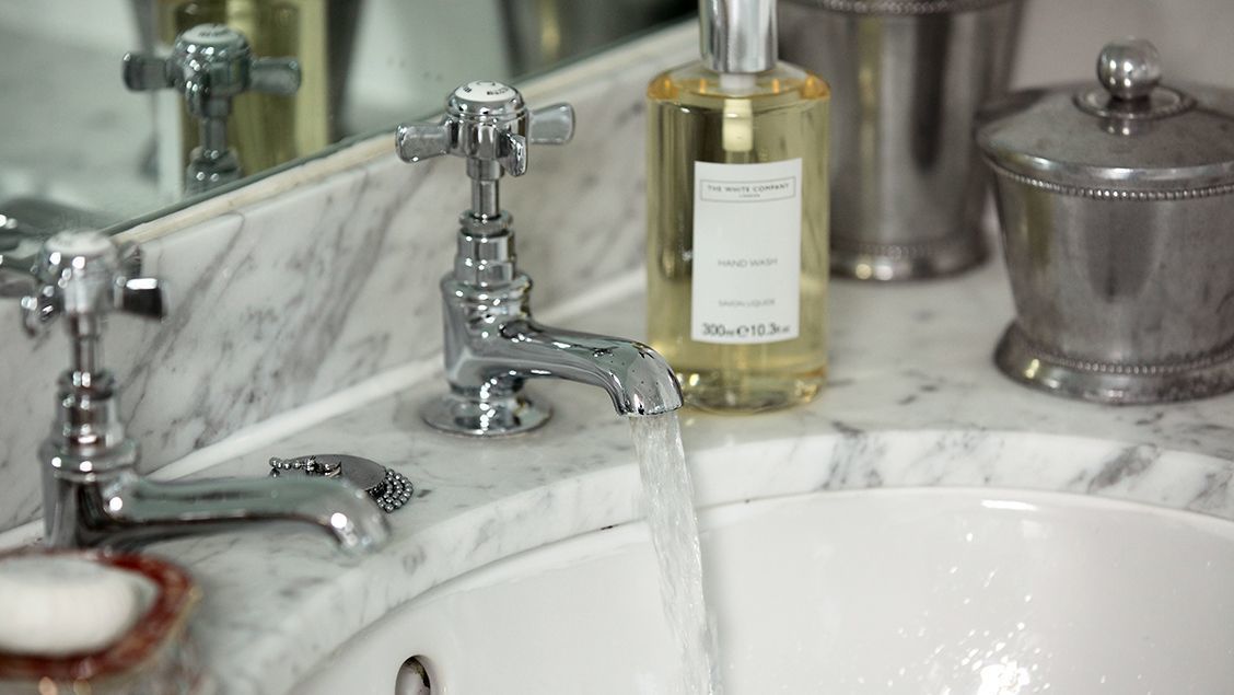 Un lavandino con l'acqua corrente, un erogatore di sapone e una bottiglia di sapone per le mani.