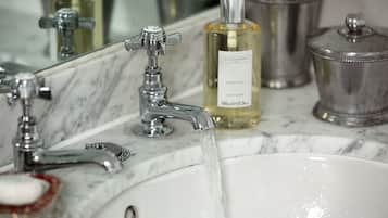 A bathroom sink with running water, a hand soap dispenser, and a bottle of hand soap.