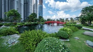 Un parc avec un étang, un pont rouge et une végétation luxuriante tout autour.