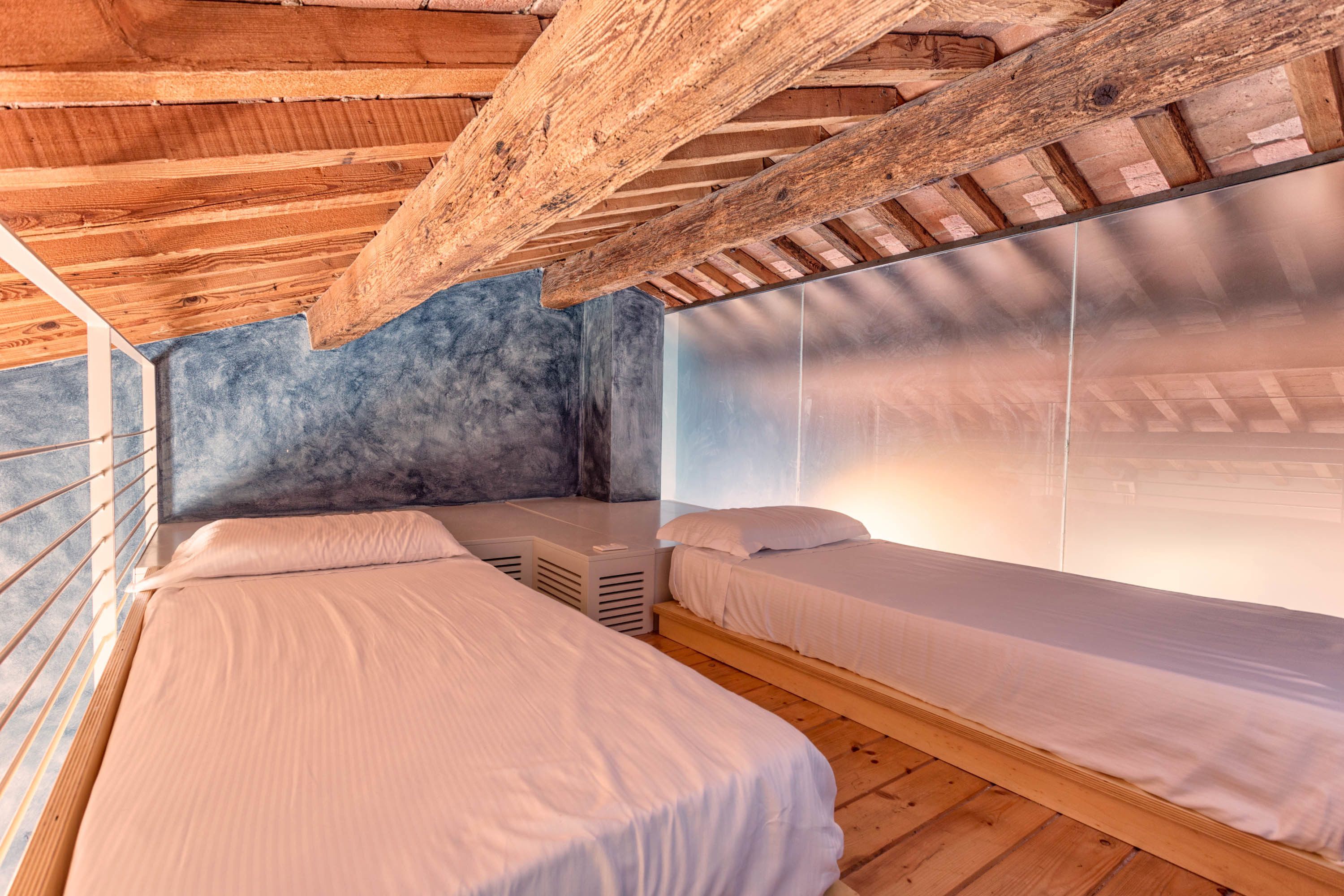 A room with two beds, wooden beams, a stone wall, and a window.