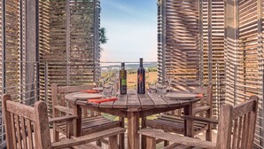 A wooden outdoor dining area with a table set for four, surrounded by wooden chairs, overlooking a vineyard.