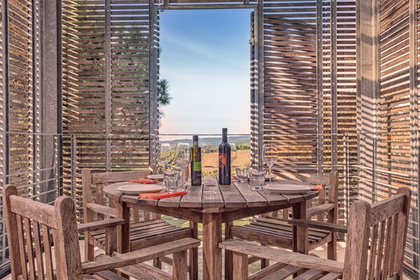 A wooden outdoor dining area with a table set for four, surrounded by wooden chairs, overlooking a vineyard. - Casale del Mare (Rosignano Marittimo)