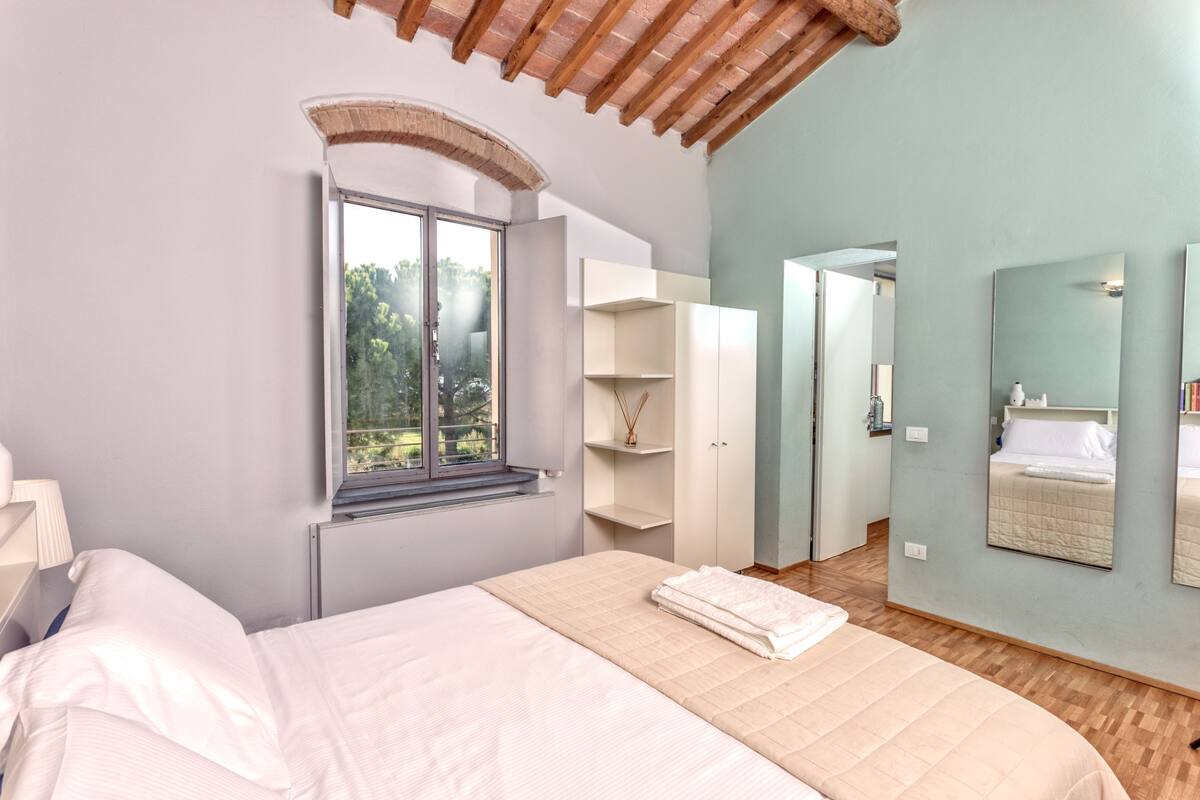 A bedroom with a bed, a window, a wardrobe, and a mirror.