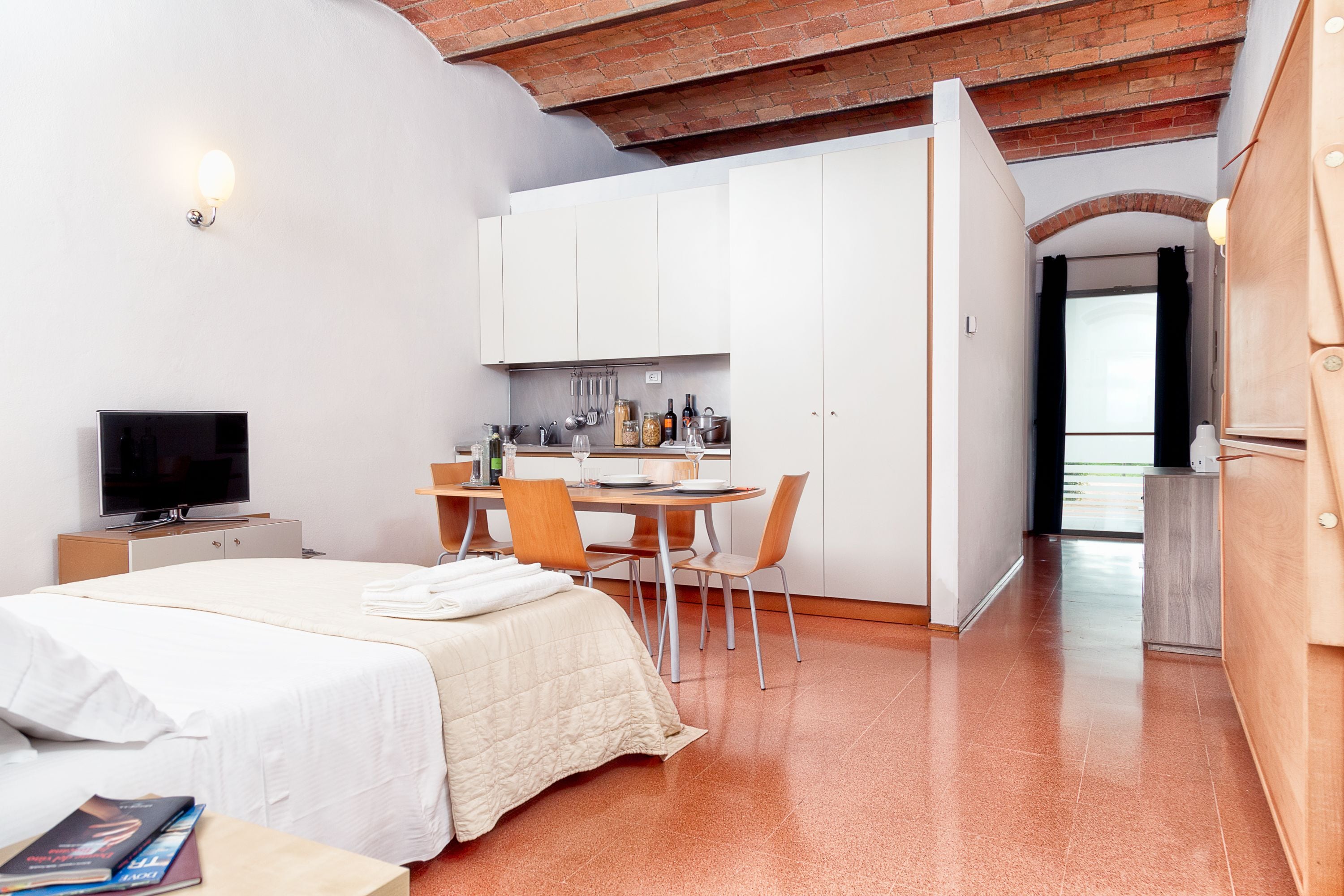 A modern hotel room with a bed, a desk, and a kitchenette.
