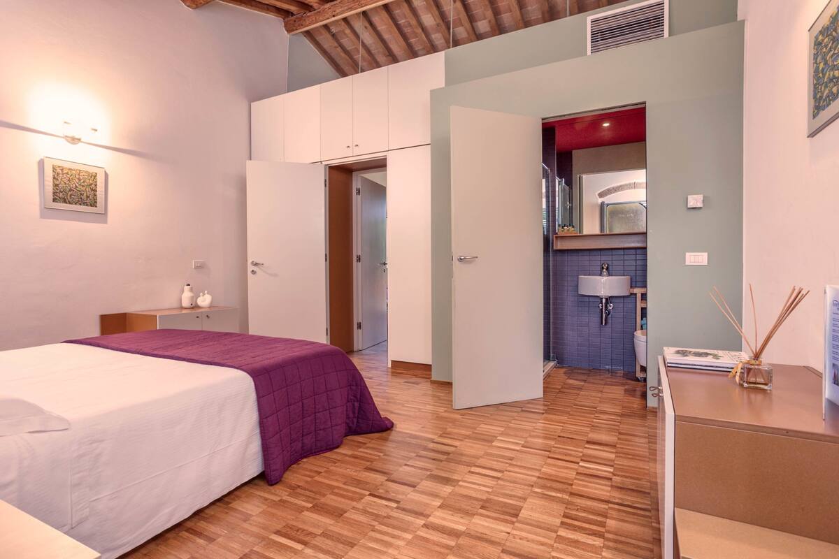 A bedroom with a bed, a wardrobe, a desk, and a bathroom visible through an open door.