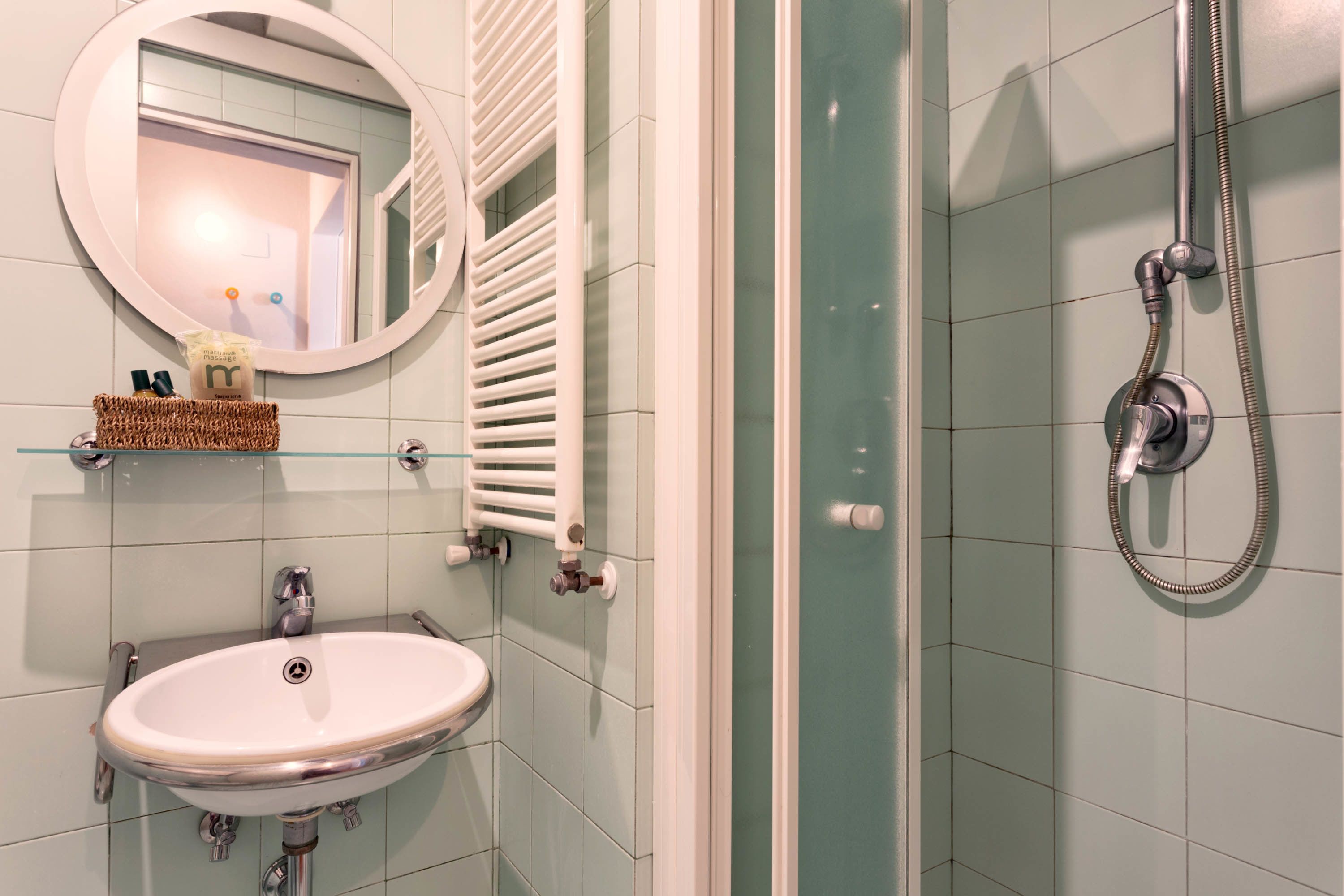 Ein Badezimmer mit einem weißen Waschbecken, einem Spiegel, einem Handtuchhalter und einer Dusche.