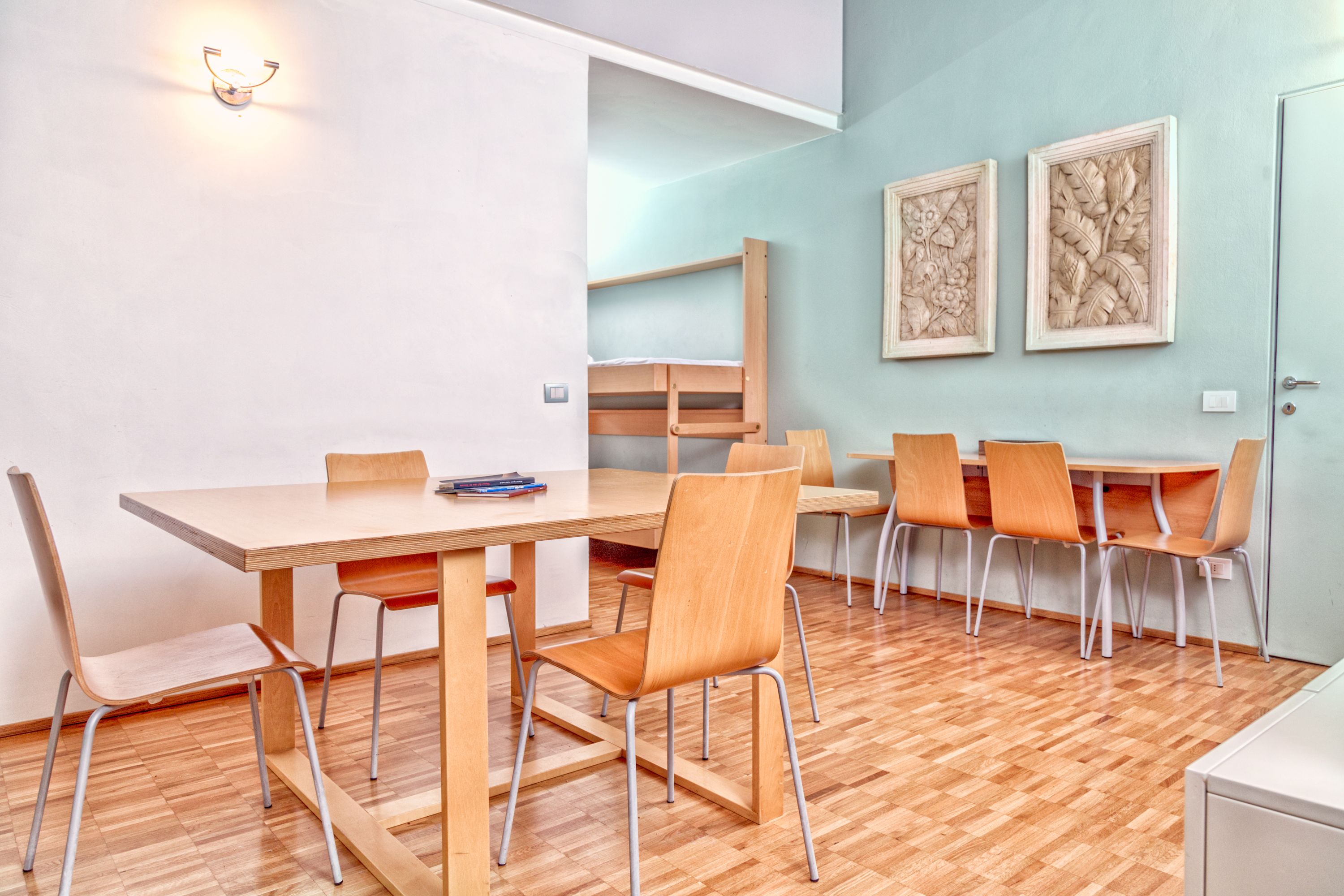 Ein moderner Essbereich mit Holztisch und -stühlen, einem Stockbett im Hintergrund und zwei gerahmten floralen Kunstwerken an der Wand.