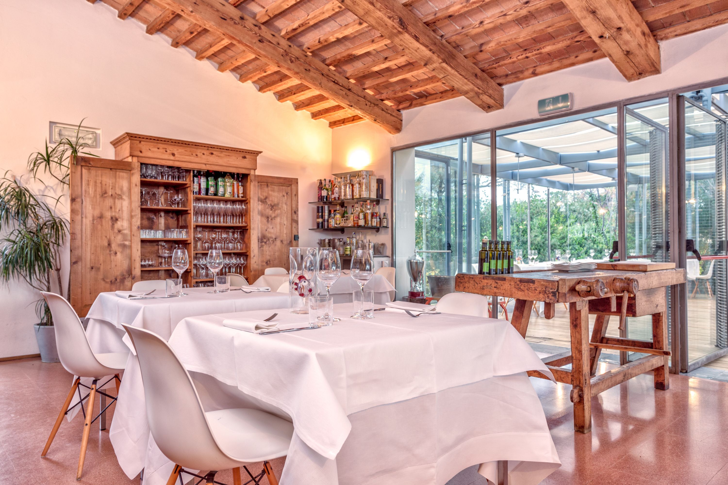 Un comedor con mesas y sillas blancas, y un mueble de madera lleno de botellas y copas.