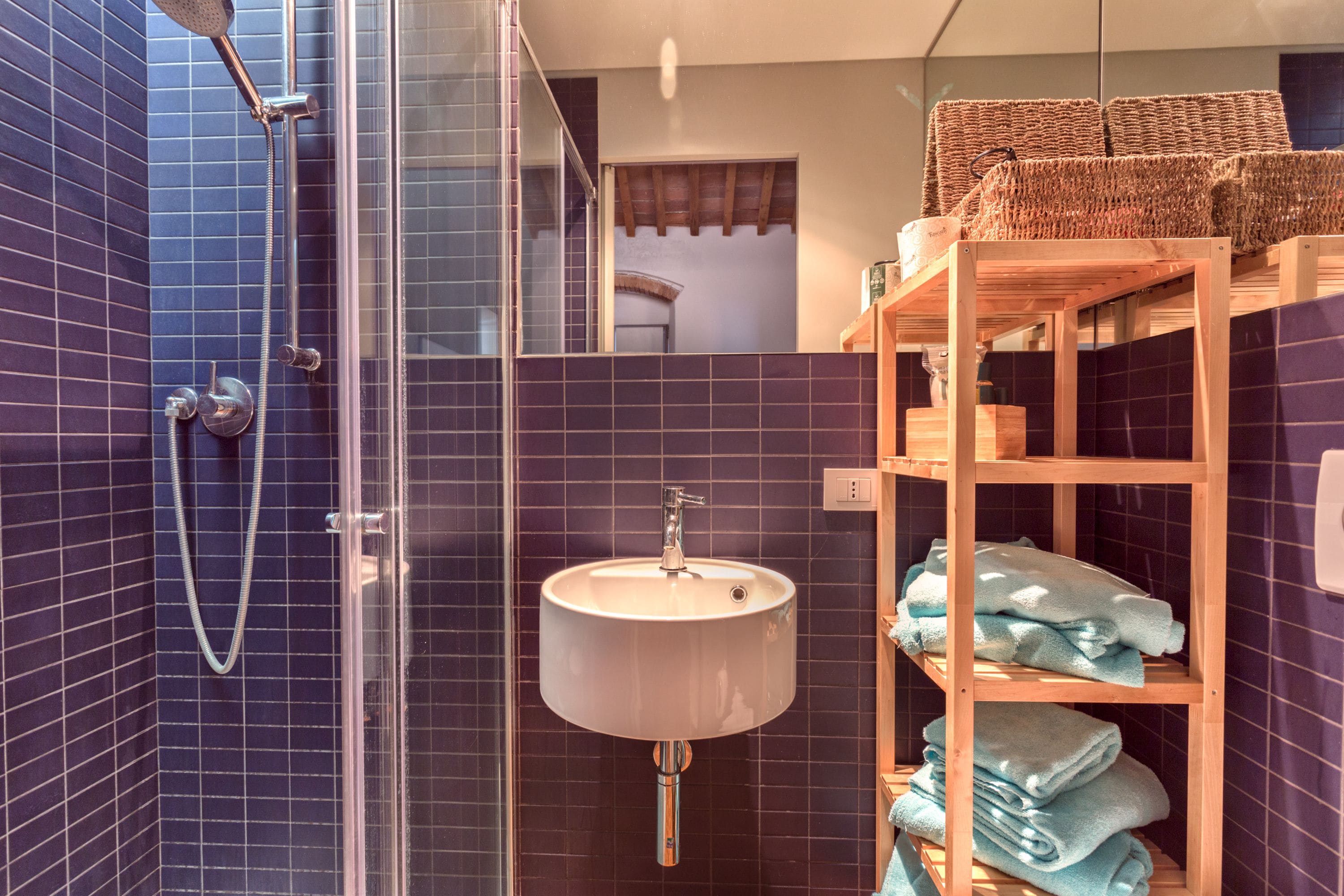 Ein Badezimmer mit Dusche, Waschbecken und einem Ablagefach mit Handtüchern.