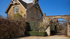 A traditional stone house with a gabled roof, a stone archway, and a gravel pathway leading to the entrance. - Goodwood Cottage (Chipping Norton)