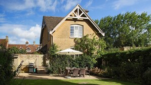 A traditional house with a pitched roof, a visible chimney, and a garden with a patio table and chairs. - Goodwood Cottage (Chipping Norton)