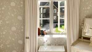 A room with a window, a table with a bottle and glass, and a lamp. - Goodwood Cottage (Chipping Norton)